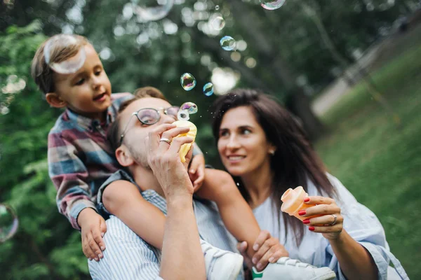 Feliz joven familia jugando con varitas de burbujas en el parque al aire libre —  Fotos de Stock