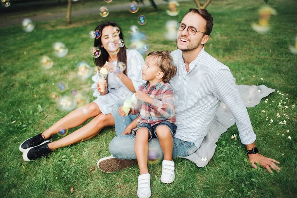 Счастливая молодая семья играет с мыльными палочками в парке на открытом воздухе — стоковое фото