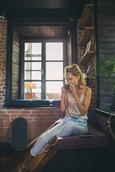 Young beautiful blonde skinny woman drinking coffee in loft — Stock Photo, Image