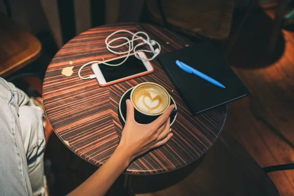 Женская рука с кофе за столом, смартфоном и ноутбуком — стоковое фото