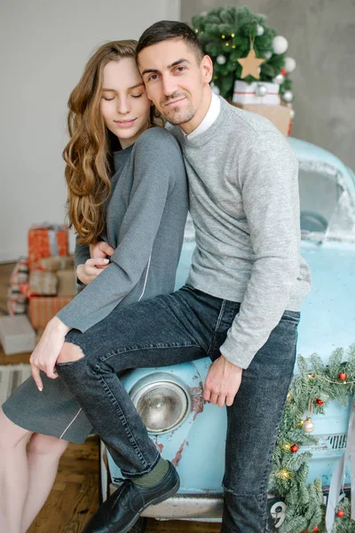 Junges Paar sitzt auf Retro-Auto in weihnachtlich dekoriertem Studio Stockbild