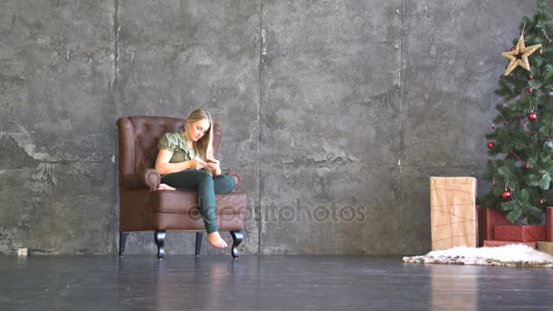 Jeune femme assise dans un fauteuil et regardant le téléphone — Video