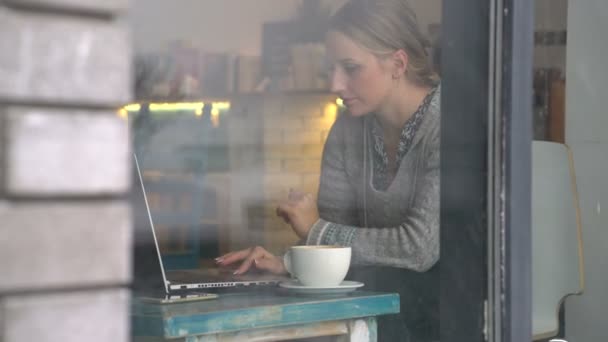 Jonge vrouw die werkt op een laptop in een café — Stockvideo