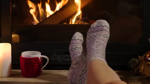 Mulher está sentada com xícara de bebida quente e reservar perto da lareira — Vídeo de Stock