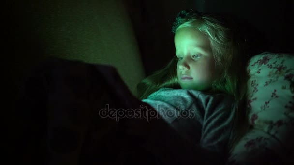 Pět let stará dívka hledá karikatury ležet na gauči ve tmě — Stock video