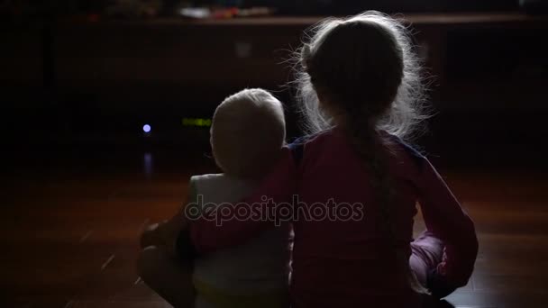 Hermano pequeño con su hermana viendo la televisión sentada en la oscuridad — Vídeos de Stock