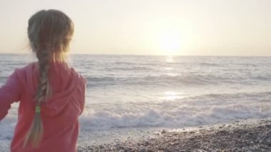 küçük kız sahilde güneşin karşılamak için çalışır ve mutlu atlar