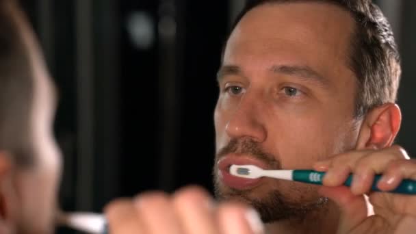 Mann mit Zahnbürste putzt Zähne und schaut in den Spiegel — Stockvideo