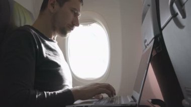 Uçağın içinde dizüstü bilgisayar kullanan genç adam