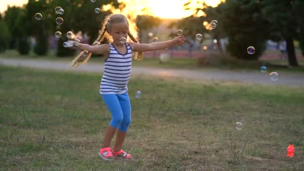 Menina brincando com bolhas no parque em um pôr do sol — Vídeo de Stock