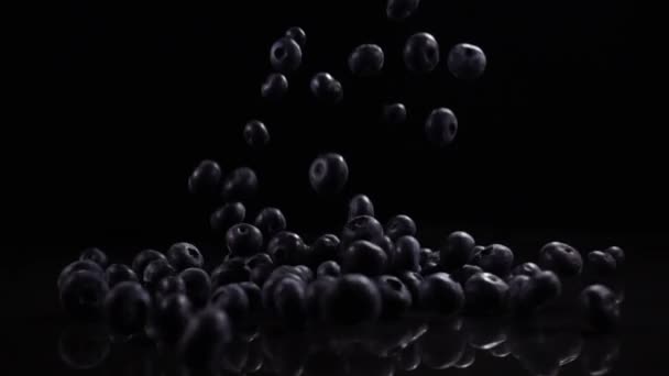 Los arándanos caen sobre una superficie sólida negra — Vídeo de stock