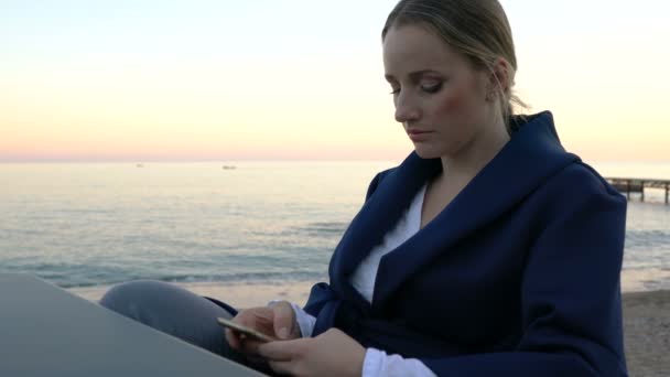 Mujer atractiva sentada en la mesa en la cafetería de la playa enviando un mensaje en el móvil — Vídeo de stock
