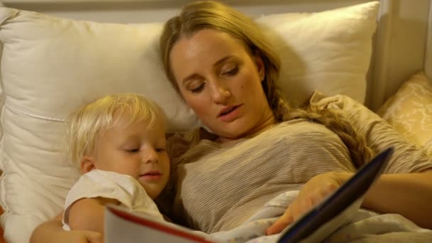 Mère et bébé fils lisant un livre au lit — Video