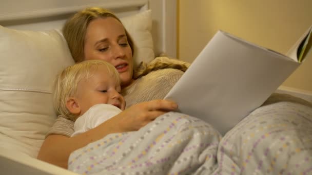 Mutter und kleiner Sohn lesen ein Buch im Bett — Stockvideo