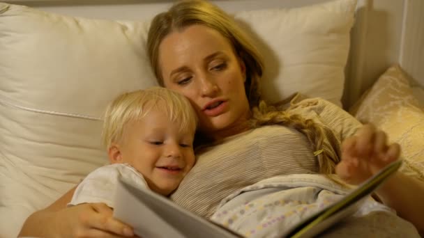 Mutter und kleiner Sohn lesen ein Buch im Bett — Stockvideo