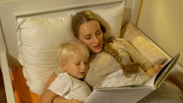 Μαμά και το μωρό ο γιος διαβάζοντας ένα βιβλίο στο κρεβάτι — Αρχείο Βίντεο