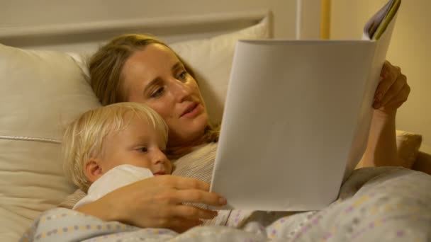 Мать и маленький сын читают книгу в постели — стоковое видео