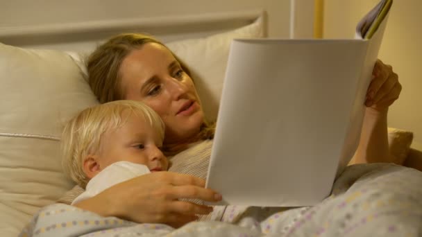 Moeder en baby zoon lezen van een boek in bed — Stockvideo