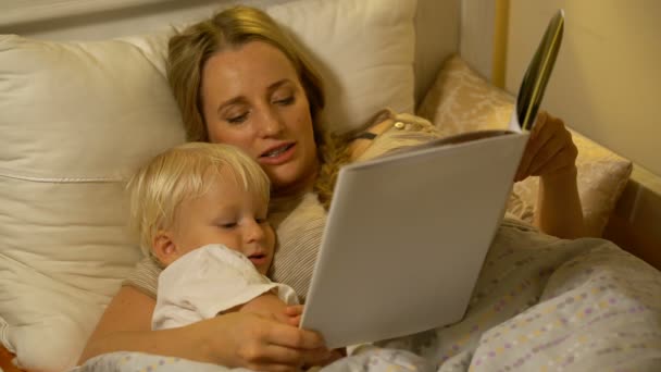Мать и маленький сын читают книгу в постели — стоковое видео