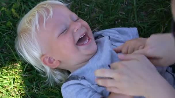 Mãe faz cócegas no bebê e ele ri deitado na grama — Vídeo de Stock