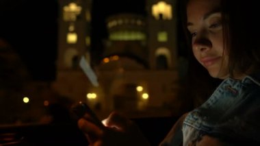 Genç bir kadın gece arabada otururken cep telefonu kullanıyor.