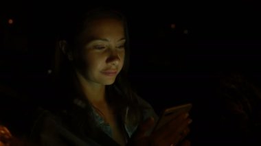 Genç bir kadın gece arabada otururken cep telefonu kullanıyor.