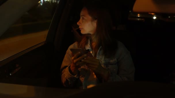 Mujer joven usando el teléfono móvil mientras está sentado en un coche por la noche — Vídeos de Stock