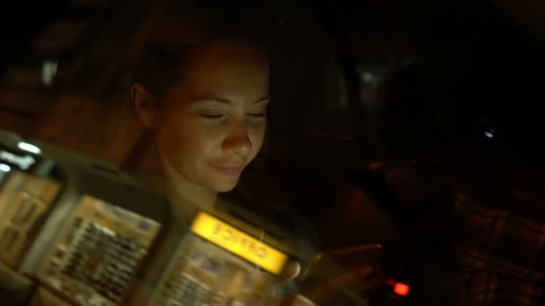 Νεαρή γυναίκα που χρησιμοποιεί κινητό τηλέφωνο ενώ κάθεται σε ένα αυτοκίνητο τη νύχτα — Αρχείο Βίντεο
