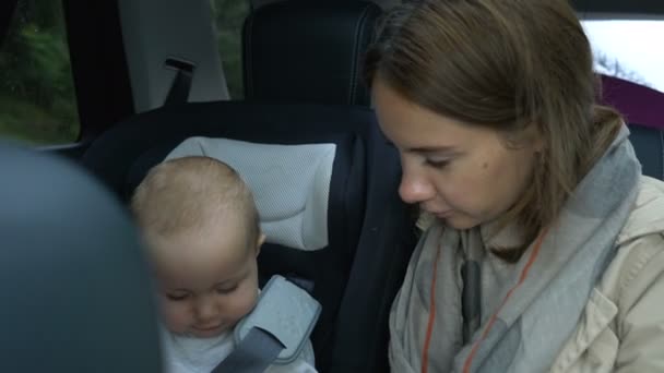 Mamá y la niña montan en el coche en el asiento trasero — Vídeos de Stock