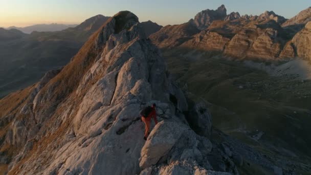 Foto épica aérea de un hombre caminando en el borde de la montaña en el hermoso atardecer — Vídeo de stock