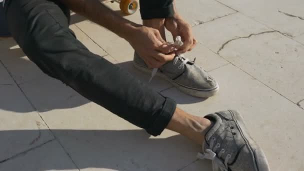 Een jonge mannelijke skateboarder bindt een kant en vertrekt dan op een skateboard — Stockvideo