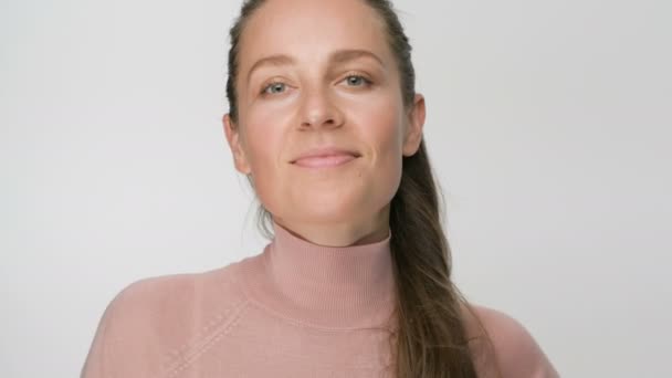 Šťastná brunetka žena ukazuje ok gesto při pohledu do kamery a úsměv přes bílé pozadí — Stock video