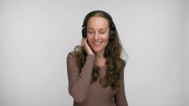 Mutlu bir kadının portresi, en sevdiği şarkıyı akıllı telefondan dinlerken, dans ederken ve müzik dinlerken beyaz arka planda kulaklıklarla eğlenirken.