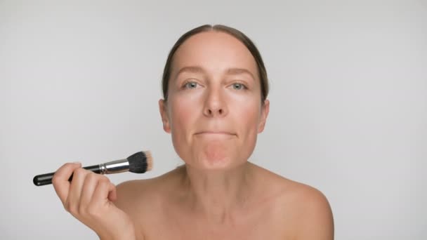Nahaufnahme Schönheit Porträt einer jungen Frau mit glatter, gesunder Haut, streichelt sie sanft die Haut mit einem Make-up-Pinsel auf weißem Hintergrund — Stockvideo