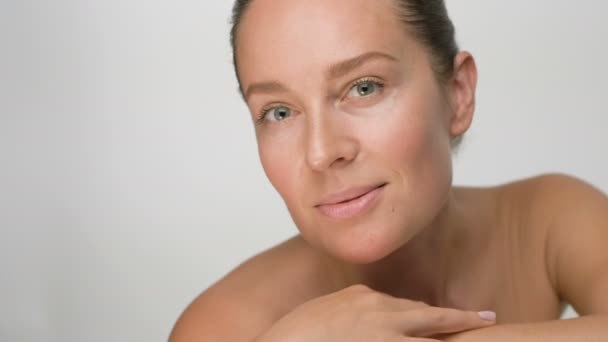 Närbild skönhet porträtt av ung kvinna med slät frisk hud, hon försiktigt vidrör ansiktet med fingrarna på vit bakgrund och leenden — Stockvideo