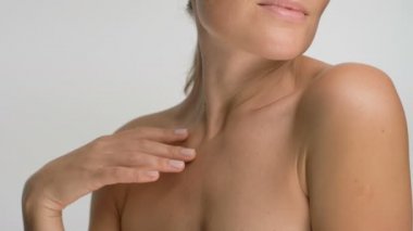 Pürüzsüz, sağlıklı bir cilde sahip genç bir kadının yakın plan güzel portresi, beyaz arka planda parmaklarıyla nazikçe omuzlarına ve yüzüne dokunur ve gülümser.