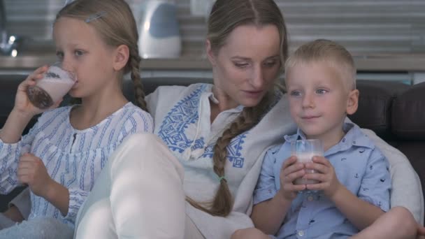 Mamma och två barn tittar på TV medan de sitter på soffan, barn dricker kakao — Stockvideo