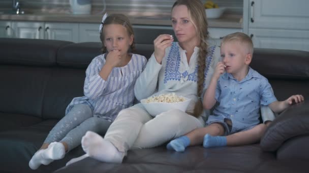 Mamma och två barn äter popcorn och tittar på TV medan de sitter på soffan — Stockvideo