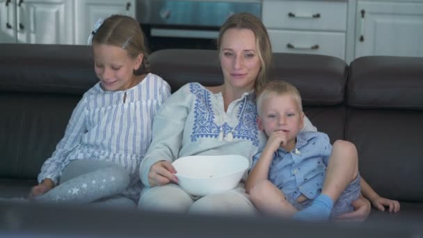 Mamma och två barn äter popcorn och tittar på TV medan de sitter på soffan — Stockvideo