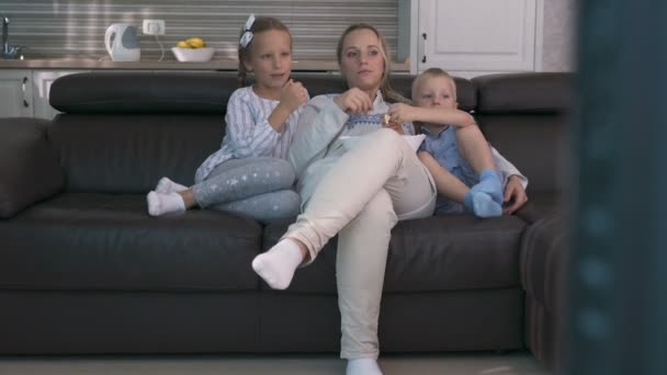 Mamma och två barn äter popcorn och tittar på TV medan de sitter på soffan — Stockvideo