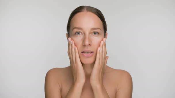 Close-up beauty portrait of young woman with smooth healthy skin, she gently touches her face with her fingers on white background and smiles — Stock Video