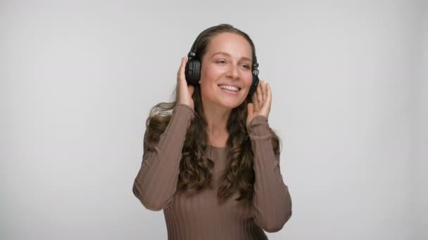 Retrato de la mujer contenta escuchando su canción favorita en el baile y el canto de teléfonos inteligentes mientras disfruta de la música con auriculares sobre fondo blanco — Vídeo de stock