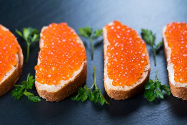 Koyu taş zemin üzerinde kırmızı havyarlı sandviçler.