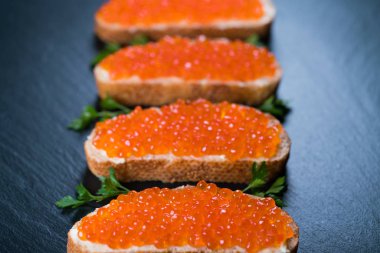 Koyu taş zemin üzerinde kırmızı havyarlı sandviçler.