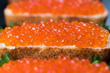 Koyu taş zemin üzerinde kırmızı havyarlı sandviçler.