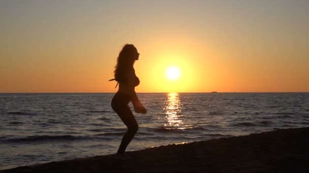 Silhouet van meisje springen bij zonsondergang aan de zeekust — Stockvideo