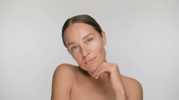 Close-up beauty portret van jonge vrouw met een gladde gezonde huid, ze zachtjes raakt haar gezicht met haar vingers op witte achtergrond en glimlacht — Stockvideo