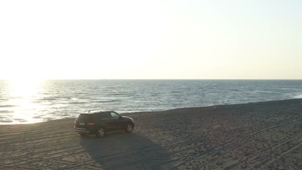 Vista aérea de um carro que se move ao longo de uma praia de areia ao longo do mar — Vídeo de Stock