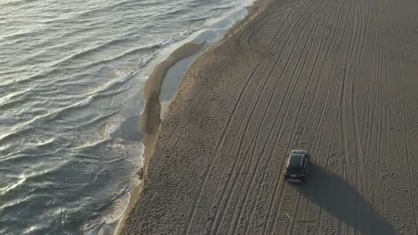 Deniz boyunca kumlu bir sahil boyunca hareket eden bir arabanın hava görüntüsü. — Stok video