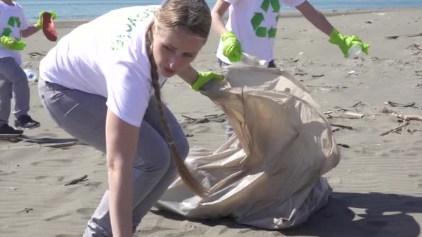 Η οικογένεια μαζεύει σκουπίδια από την παραλία σε σακούλες σκουπιδιών. — Αρχείο Βίντεο